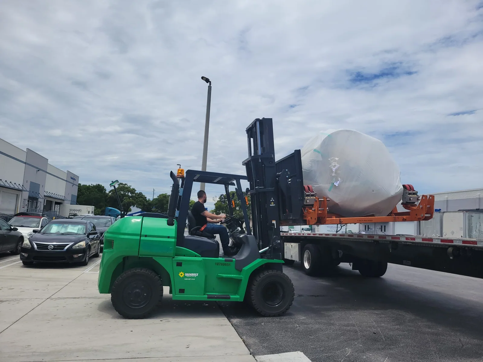 Forklift positioning a wrapped aerospace component on a flatbed trailer.