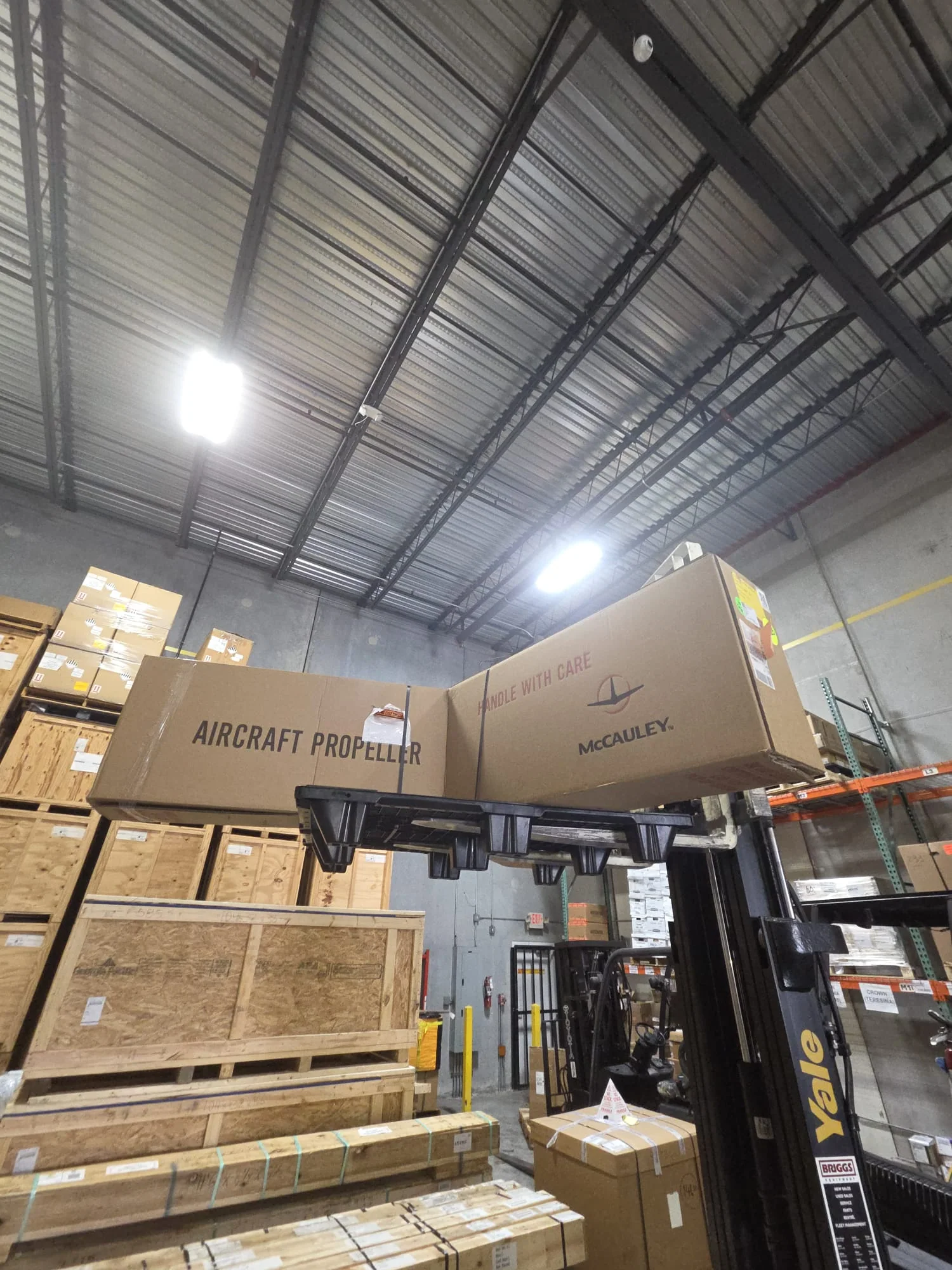 Forklift moving a pallet of long aircraft propeller packages inside a warehouse.