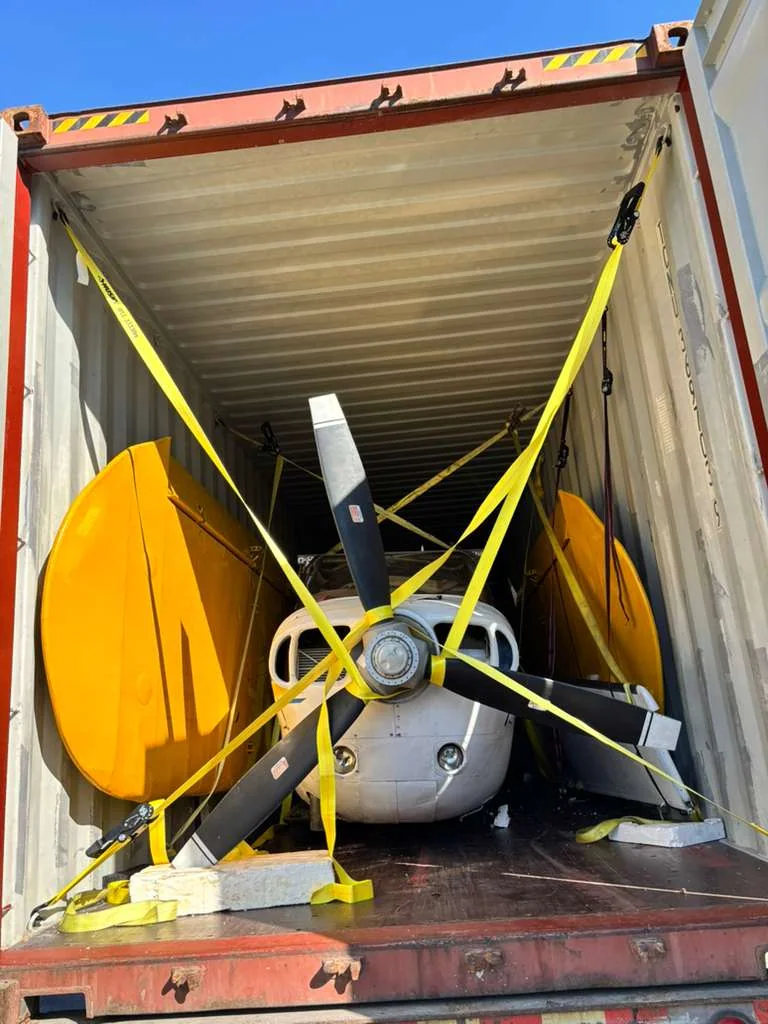 Front of a small propeller aircraft secured inside a shipping container.