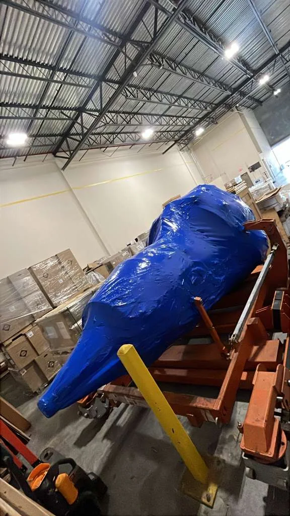 Large aerospace component protected with blue wrapping inside a warehouse.