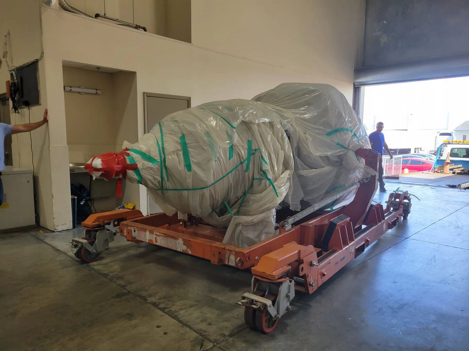 Large wrapped component on a transport base near a loading door.