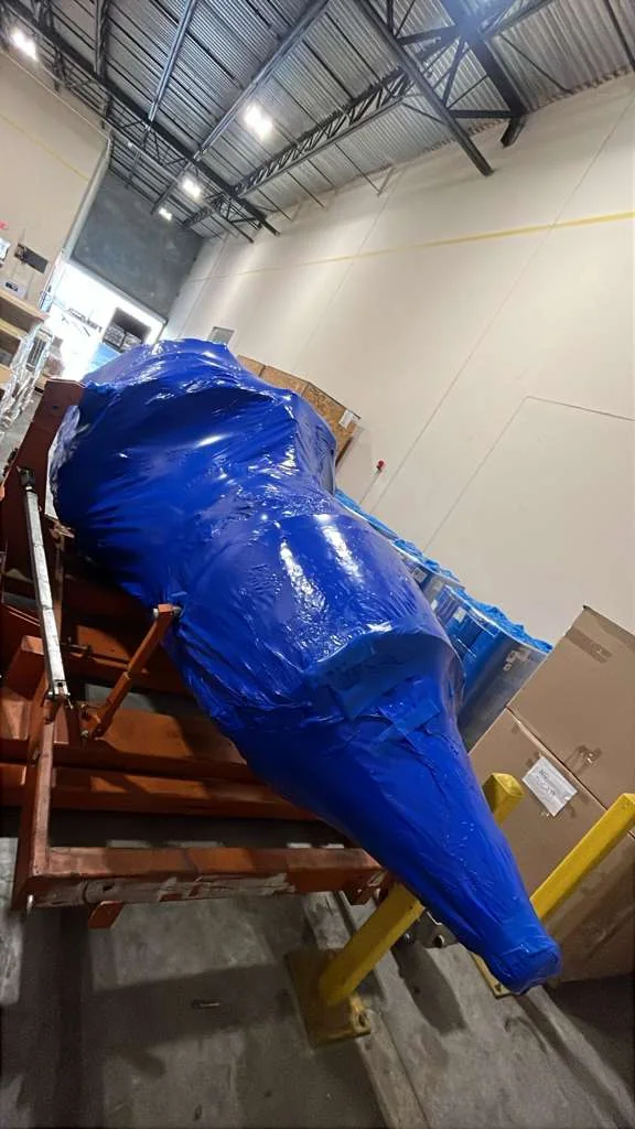 Blue-wrapped aerospace component supported inside a warehouse.