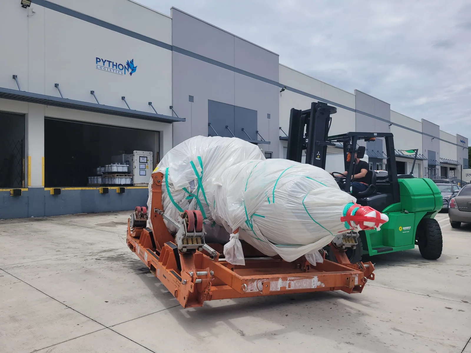 Forklift beside a wrapped component on a transport frame.