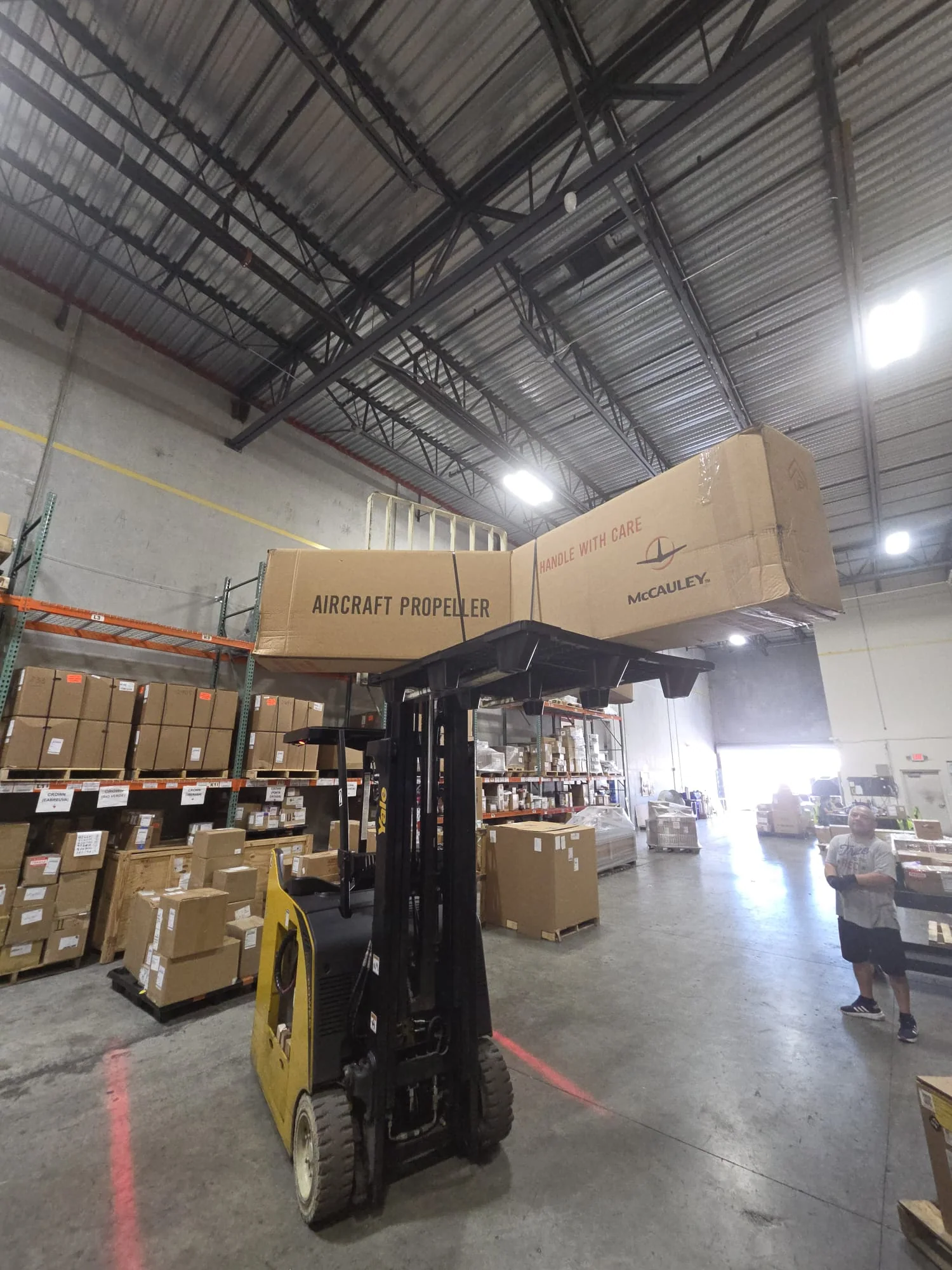Forklift carrying long packaged components through a warehouse.