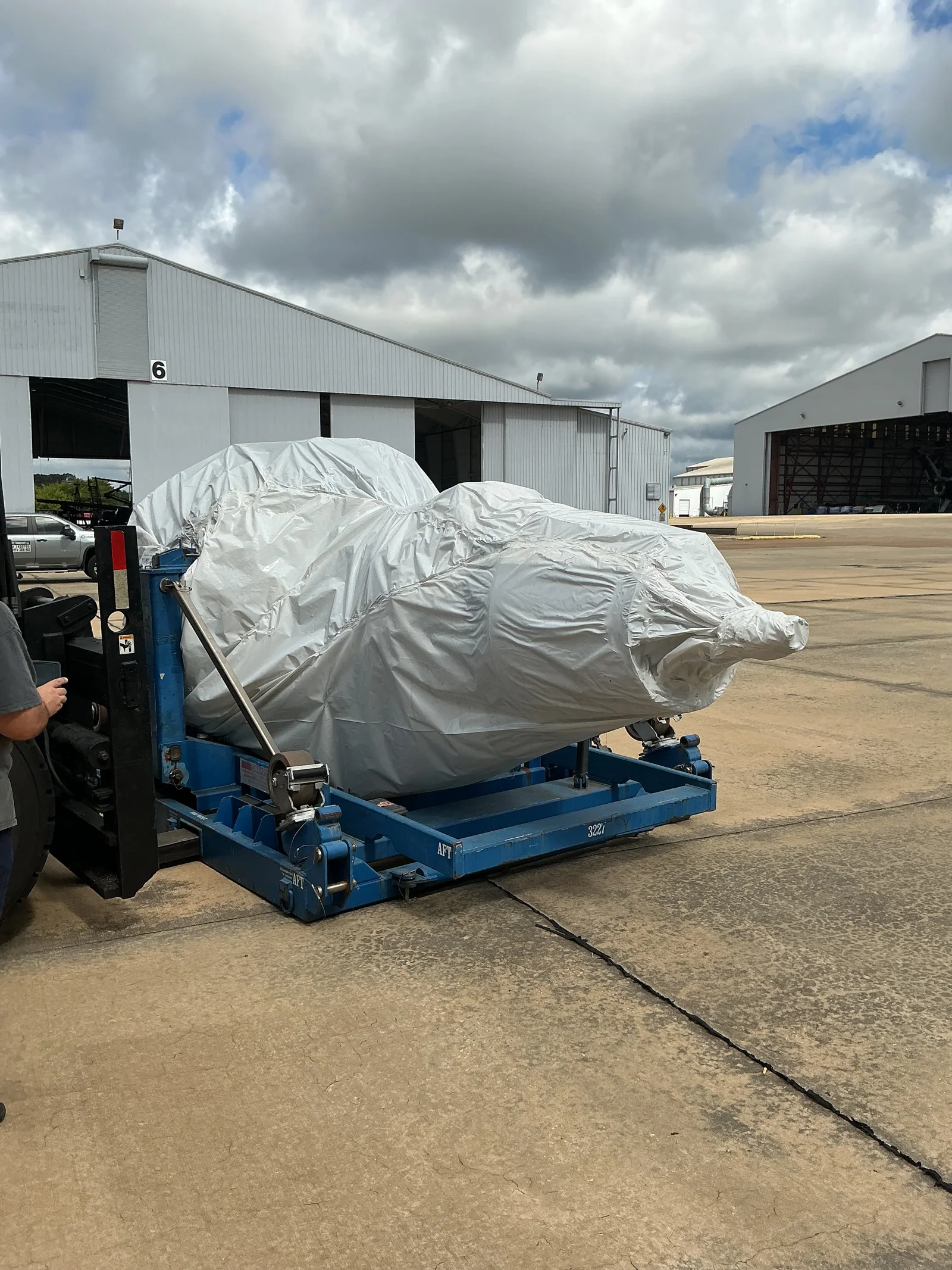 Wrapped aerospace component on a blue transport frame beside a forklift.