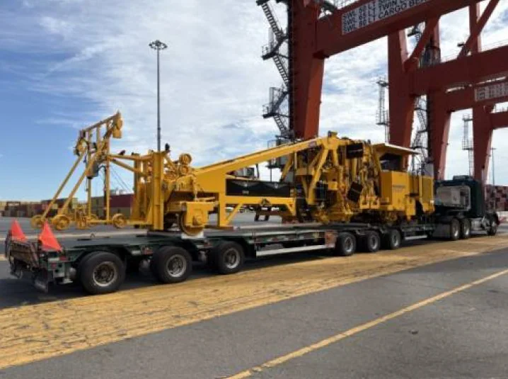 Yellow railway equipment on a long road trailer in a port area.