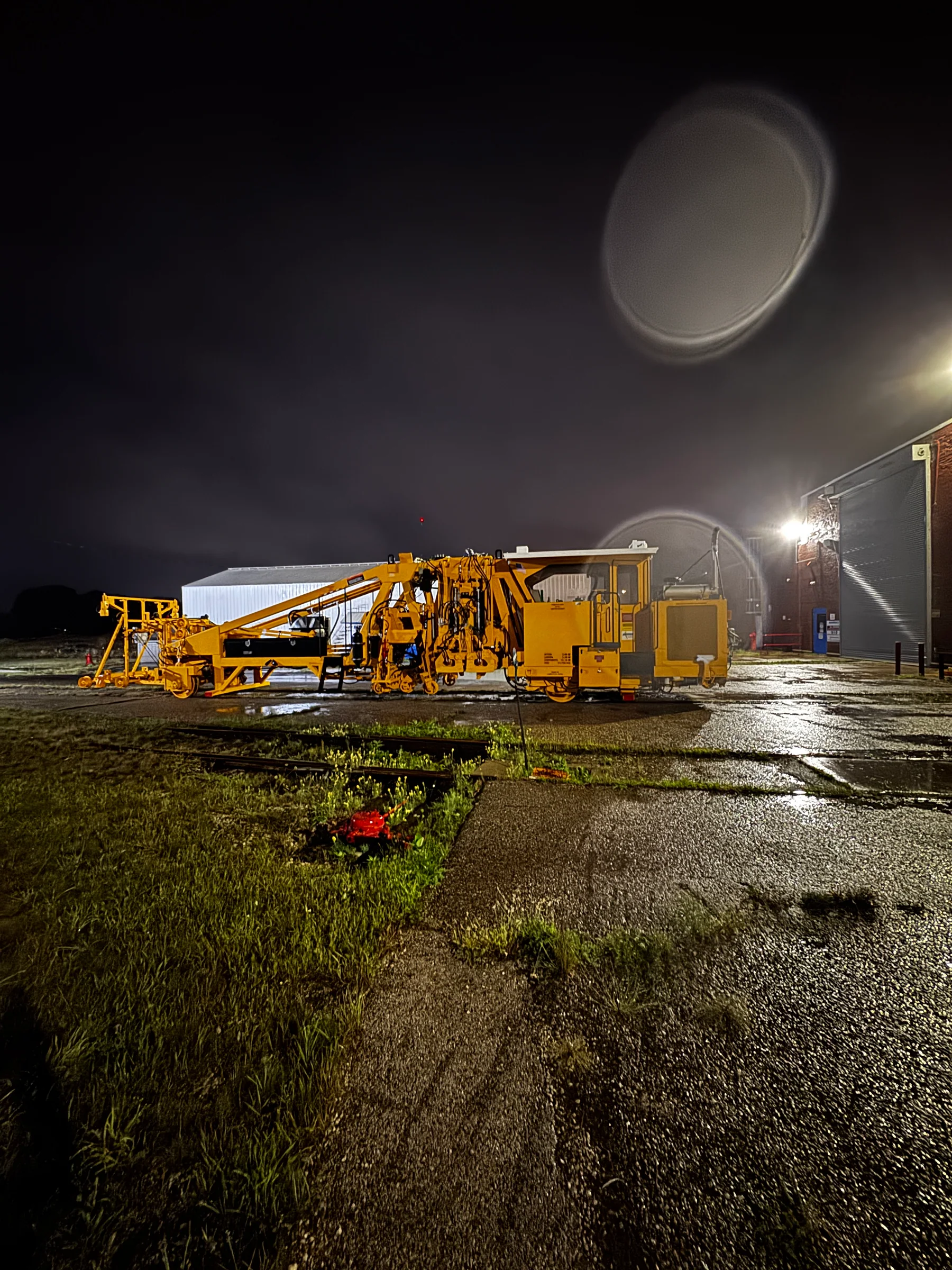 Yellow railway equipment outdoors at night beside an industrial building.