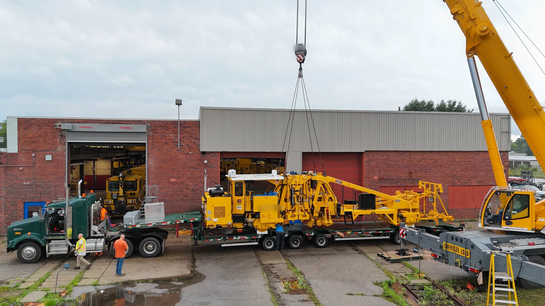 Wide view of yellow railway equipment on a road trailer next to a mobile crane.