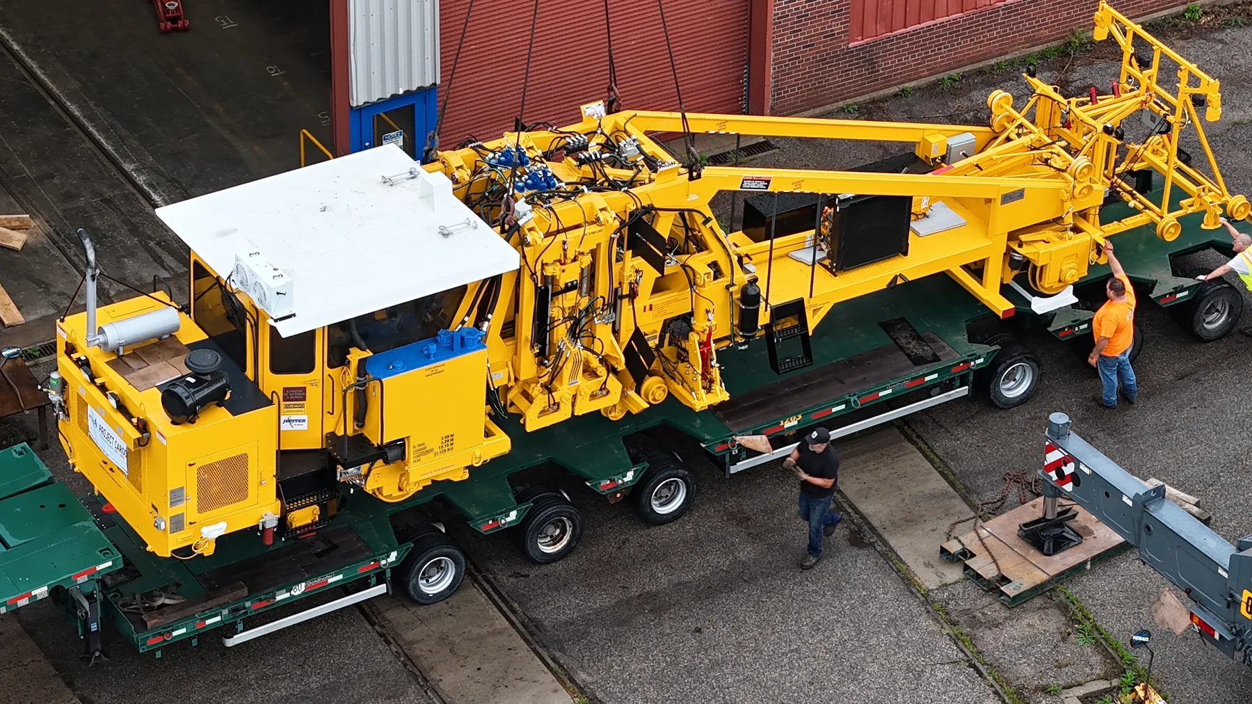 Aerial close view of yellow railway equipment suspended above a green road trailer.